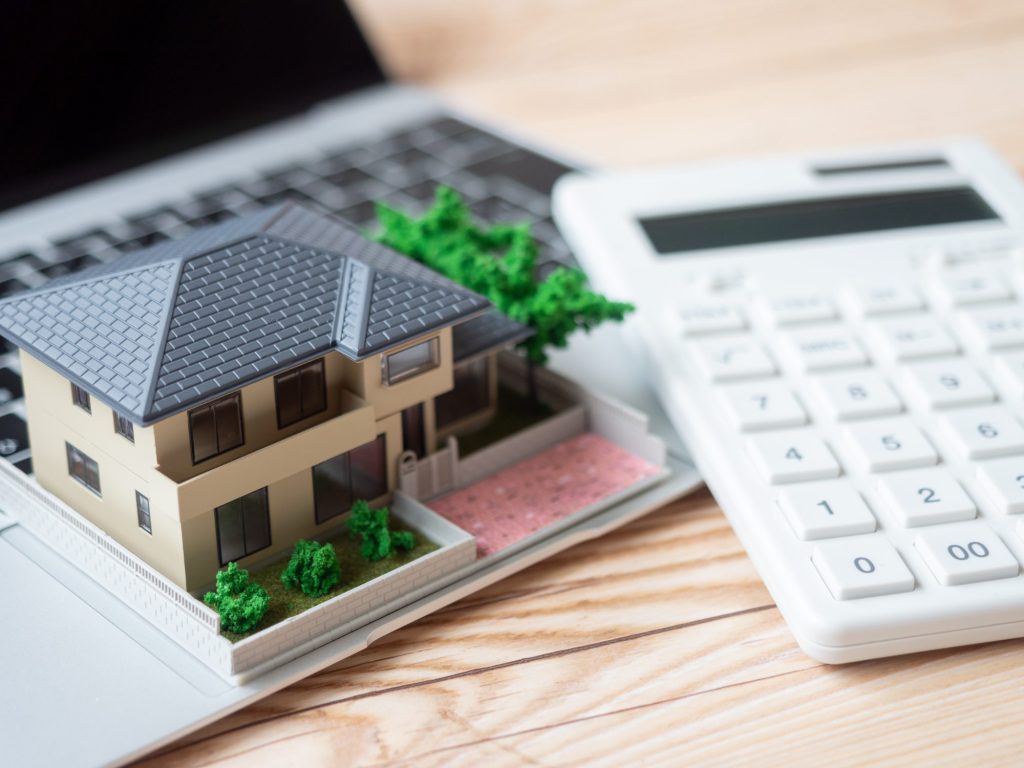 住宅模型と電卓を使って住宅購入の資金計画を考えるイメージ